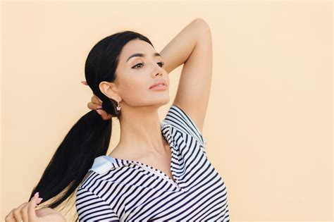 Sideways Shot Of Good Looking Brunette Woman Keeps Hair In Pony Tail