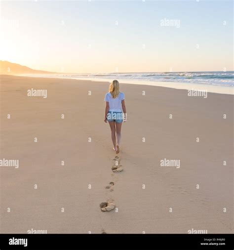 Lady Walking On Sandy Beach In Sunset Leaving Footprints Behind Stock