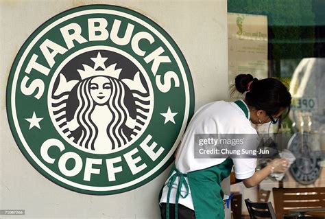 A Starbucks Worker Cleans The Window Next To A Company Logo At A