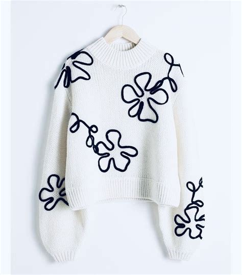 A White Sweater With Black And White Flowers On The Front Hanging From