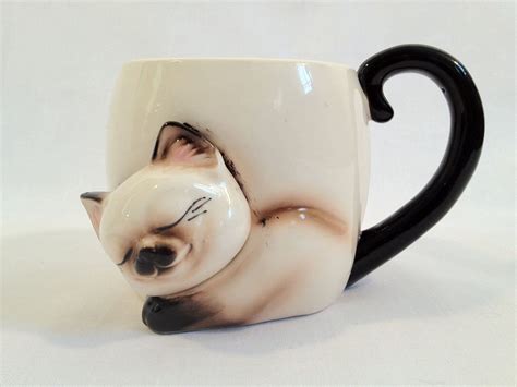 A White And Black Coffee Cup With A Cat On It S Face In The Shape Of A Mug