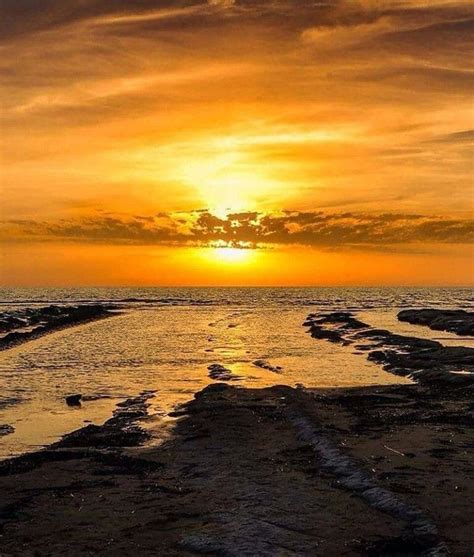 The Sun Is Setting Over The Water On The Beach