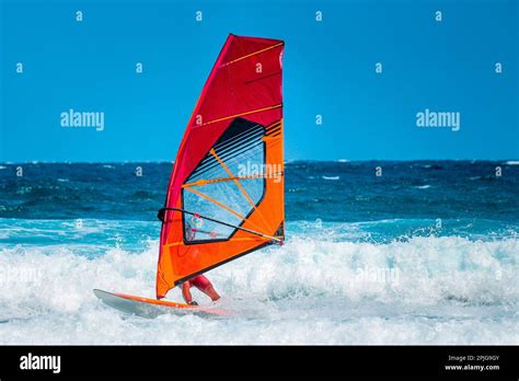 Water Sports Windsurfer With Red And Orange Sail Riding The Waves