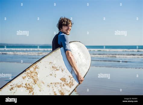 Handsome Sporty Young Surfer Posing With His Surfboard Under His Arm In His Wetsuit On A Sandy