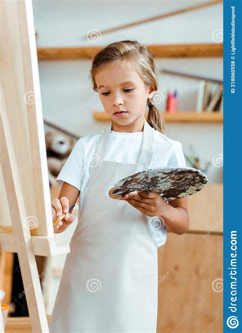 Kid In Apron Holding Palette With Colorful Gouache Paint And Paintbrush