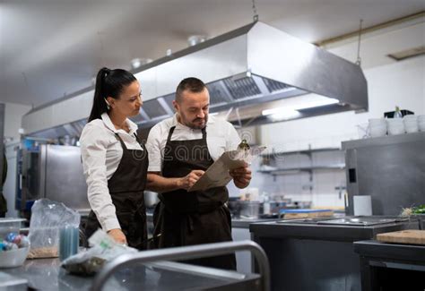 Chef And Cook Discussing Menu Indoors In Restaurant Kitchen Stock