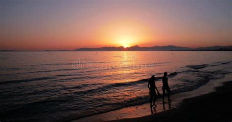 Silueta De Gente Caminando Por La Playa Al Atardecer Imagen De Archivo