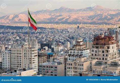 Aerial View Of Tehran Skyline At Sunset With Large Iran Flag Waving In