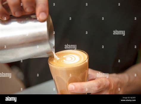 Close Up Of Baristas Hands Pouring Milk Into Coffee In Cafe Stock