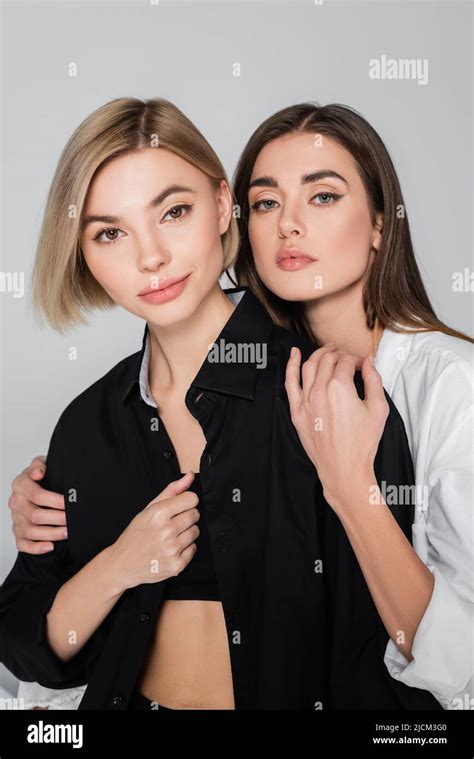 Brunette Woman Embracing Smiling Blonde Friend While Looking At Camera