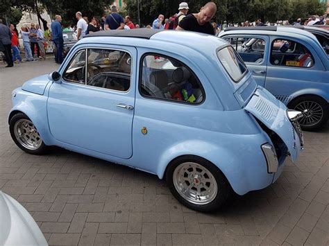 An Old Blue Car Is Parked On The Side Of The Road With People Looking At It