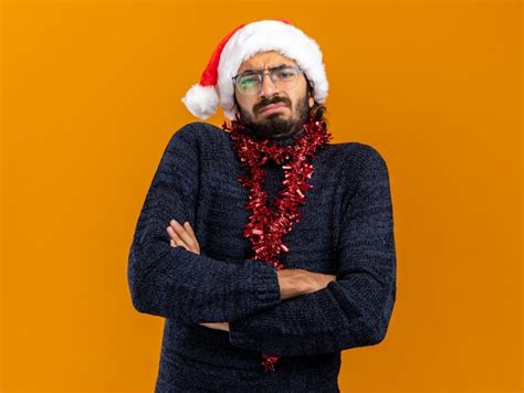 Fruncir el ceño joven guapo con sombrero de navidad con guirnalda en el