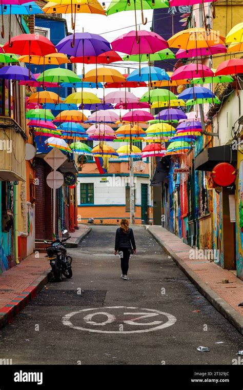 Tourist Walks Down A Street Decorated With Colorful Umbrellas In Bogota