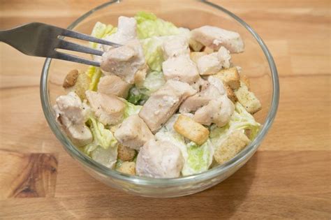 A Glass Bowl Filled With Chicken And Lettuce On Top Of A Wooden Table