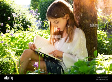 Niña RECOSTADA contra el tronco del árbol leyendo un libro Fotografía