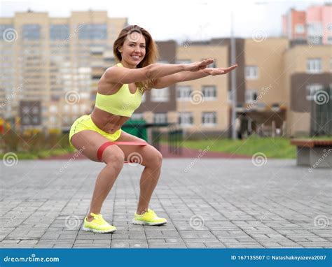 Caucasian Fit Smiling Girl Do Squats With Elastic Band Outdoor On