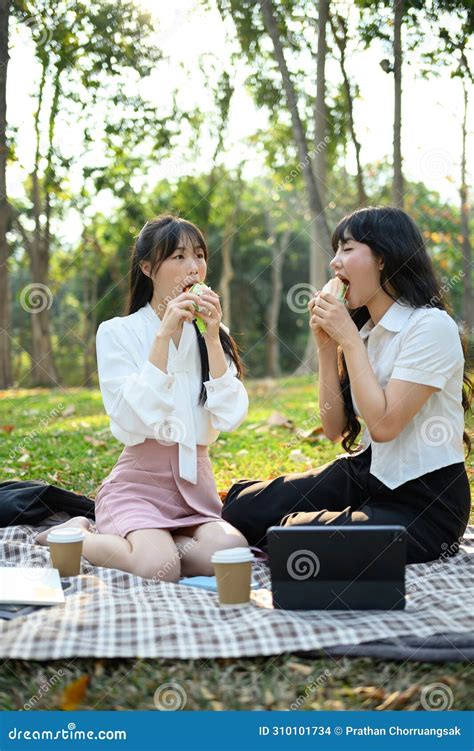 Cheerful Female Colleagues Enjoying Sandwich During Lunch Break At