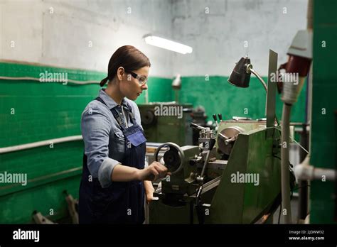 Concentrated Brunette Woman In Overall Working With Metal Punching Machine While Processing
