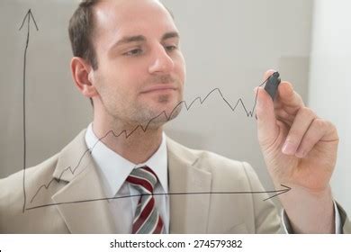 Businessman Drawing Graph On Glass Panel Stock Photo