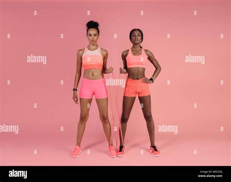 Two Women Doing Exercises With Resistance Band Over Pink Background