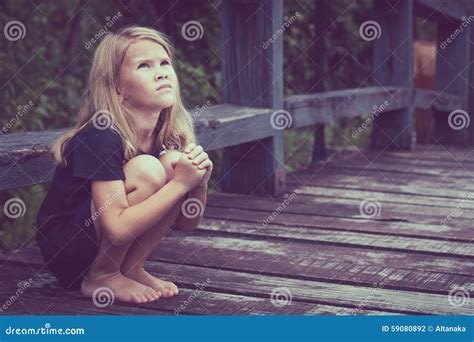 Portrait De La Petite Fille Blonde Triste S Asseyant Sur Le Pont Photo