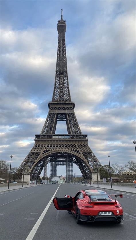 A Red Sports Car Parked In Front Of The Eiffel Tower