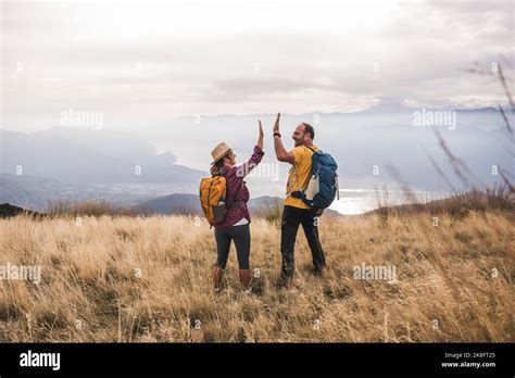 Happy Mature Man Giving High Five To Woman Standing On Grass Stock