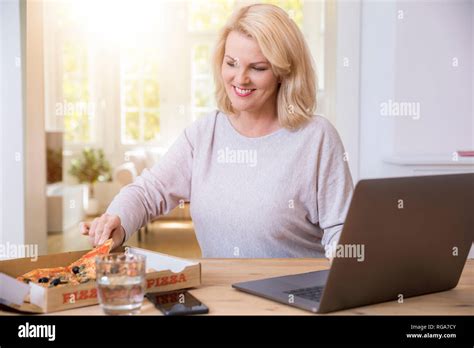 Portrait Smiling Blond Mature Woman Home Office Eating Pizza Hi Res