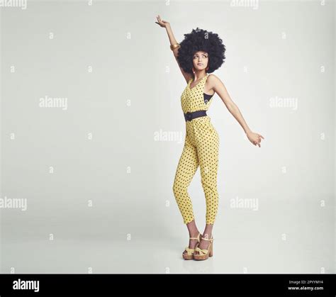 Lets disco. A young woman wearing a 70s retro jumpsuit and striking a disco pose while in the ...