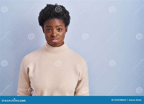 African American Woman Standing Over Blue Background Puffing Cheeks