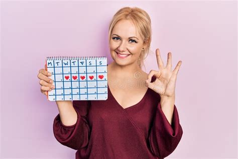 Jeune Femme Blonde Tenant Le Calendrier De Coeur Faisant Ok Signe Avec Les Doigts Souriant