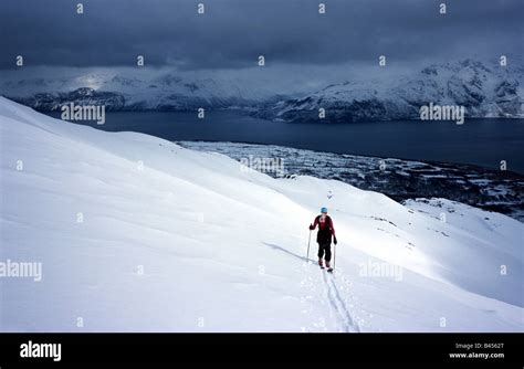 Skier Climbing A Mountain In Sunshine With Storm Clouds Coming In Over