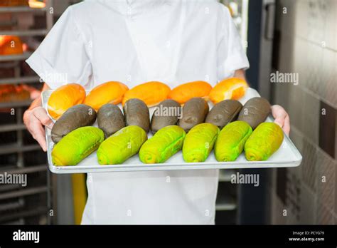 The Baker Is Holding Fresh Multicolored Buns In The Background Of The