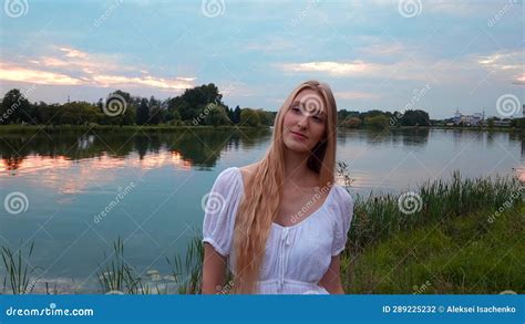 Young Woman In Long White Dress Standing On The River Bank During