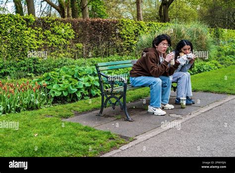 Asian Couple Eating On A City Park Bench In Spring Sunshine Concept