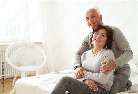 Mature 60 Year Old Couple Hugging While Sitting On The Bed In The Bedroom Love Forever Stock