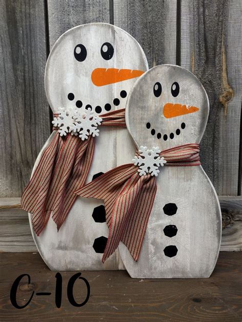 Two Snowmen Are Standing Next To Each Other In Front Of A Wooden Fence