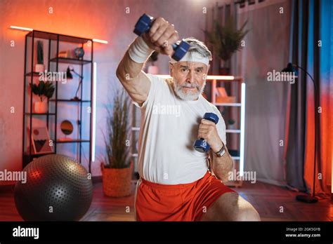 Muscular Mature Man In Sportswear Using Dumbbells For Training Arms At