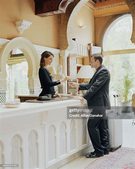 Hotel Receptionist Greeting Businessman Handing Key Over Desk High Res