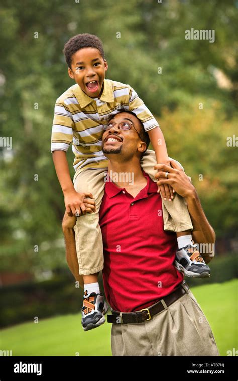 Father Carrying His Son On His Shoulders Smiling And Looking At