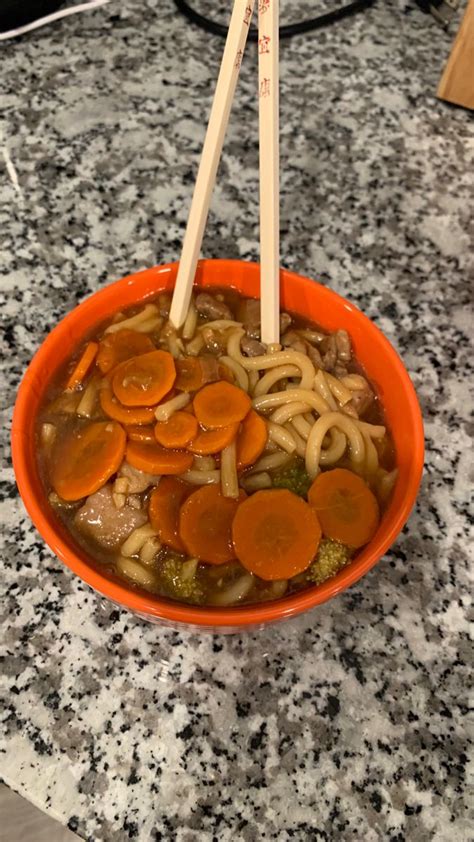 An Orange Bowl Filled With Noodles And Carrots