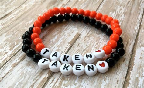 Two Bracelets With The Words Taken Written In White And Black Beads On An Old Wooden Table