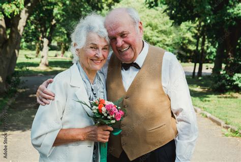 Old Couple Is Walking In The Green Park Grandmother And Grandfather At Their Golden Wedding