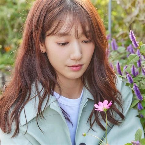 A Woman With Long Red Hair Standing In Front Of Purple Flowers