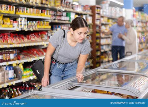 Female Buyer Carefully Chooses Frozen Food In Grocery Store Freezer