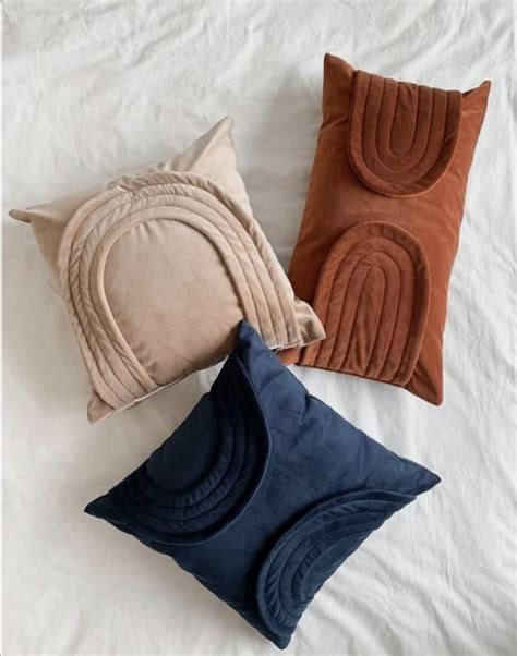 Three Pillows On A Bed With White Sheets And Brown Blue And Tan Colors