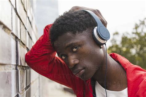 Young Black Man Leaning On Wall Listening Music With Headphones Stock