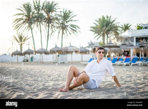 Portrait Of Handsome Man Sitting Relaxed On The Beach By Sunset Stock