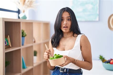 Brunette Woman Eating A Salad At Home In Shock Face Looking Skeptical