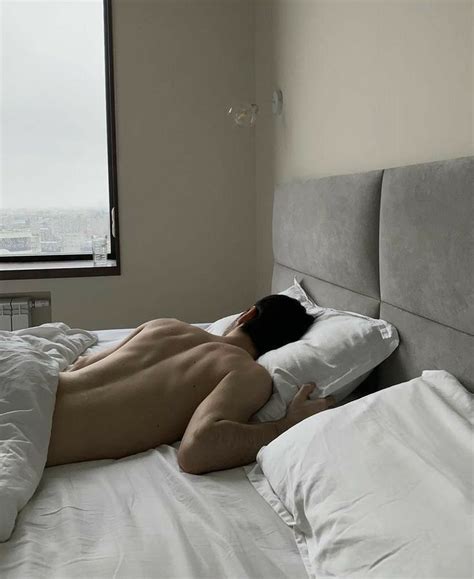 A Naked Man Laying On Top Of A Bed Next To A Window